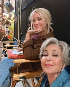 two women are sitting in chairs and one is looking at the camera with her hand on her chin