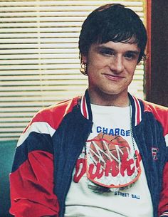 a young man sitting in front of a window wearing a red, white and blue jacket