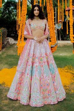 a woman in a pink and blue lehenga standing under orange flower garlands