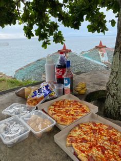 three pizzas and drinks on a picnic table by the ocean with water in the background