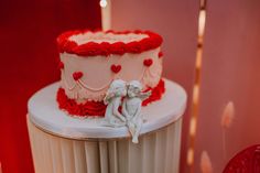 there is a wedding cake with red and white frosting on the top that has two cherubs sitting next to it