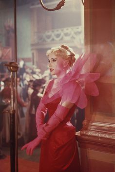 a woman in a red dress standing next to a clock with people looking on from behind it