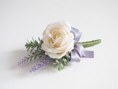 a white rose and lavender ribbon boutonniere on a white background with greenery