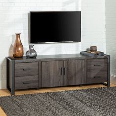 a flat screen tv sitting on top of a wooden cabinet next to a vase and lamp