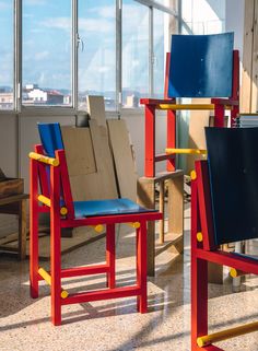 two chairs with different colors and shapes in front of large windows, one blue and the other red