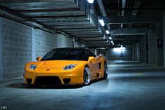 a yellow sports car parked in a parking garage with its hood up and lights on