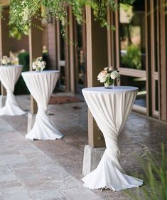 two tables with white tablecloths and flowers on them are lined up in front of a building