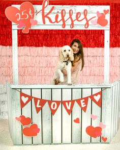 a woman holding a white dog in front of a valentine's day photo booth