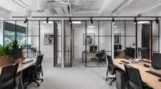 an office with multiple desks and chairs in front of glass partitions that divide the space