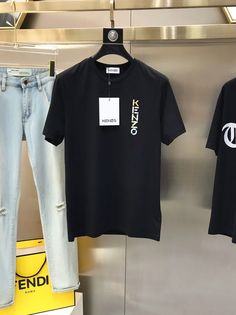 two black tshirts hanging on a metal rack in front of a yellow box