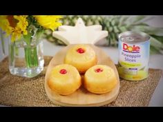 three pineapple slices on a wooden plate next to a vase with yellow flowers and a can of pineapple slices