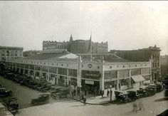 an old black and white photo of cars parked in front of a building with tall buildings