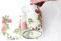 a person is holding a glass jar with flowers on it and another hand reaching for the top