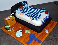 a cake shaped like a child laying on a bed with clothes and toys around it