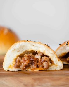 two pieces of bread with meat in it on a wooden table next to buns