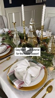 the table is set for christmas dinner with gold and white plates, silver candlesticks, and evergreen garland