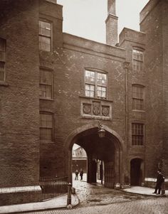 an old black and white photo of people standing in front of a brick building with arched doorways