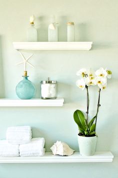 two white shelves with towels, vases and flowers on them in a bathroom setting