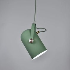 a green lamp hanging from the ceiling on a gray wall with a light bulb attached to it