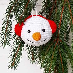 a crocheted snowman ornament hanging from a pine tree with needles