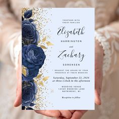 a person holding up a wedding card with blue roses on the front and gold leaves on the back