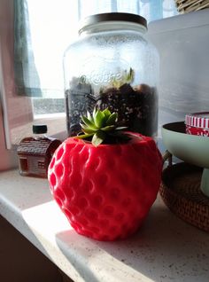 a red strawberry shaped planter sitting on top of a counter next to a glass jar