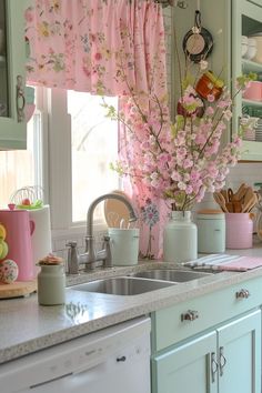 a kitchen with pink flowers in vases on the window sill and green cabinets