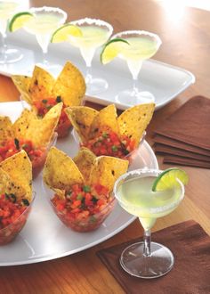 small cups filled with salsa and tortilla chips on a plate next to a margarita