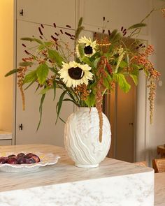 a white vase filled with lots of flowers on top of a marble table next to a plate