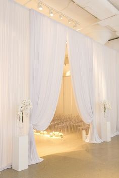 an empty room with white drapes and flowers