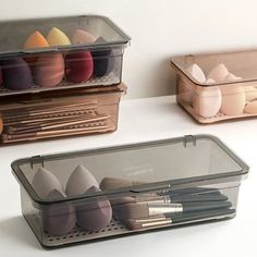 three plastic containers with different types of makeup brushes in them and one is holding an egg