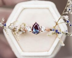 a close up of a ring in a box with flowers on the side and a blue stone