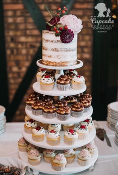 a tiered cake with cupcakes and flowers on the top is surrounded by other desserts