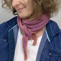 a woman with curly hair wearing a pink knitted cowl scarf and denim jacket