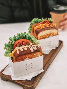 two sandwiches with lettuce, tomato and cheese on a wooden tray next to a cup of coffee