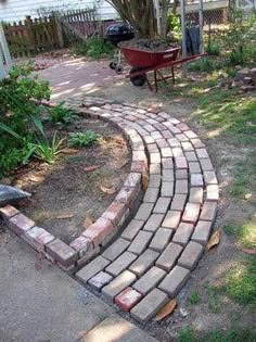 a brick path in the middle of a yard with a wheelbarrow behind it