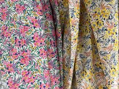 two different colored floral fabrics hanging on a rack with the same fabric in front of them