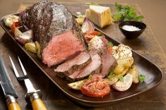 a plate with meat, potatoes and tomatoes on it next to a knife and fork