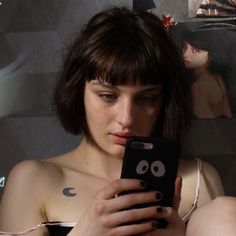 a woman is looking at her cellphone while sitting in front of a wall with pictures on it