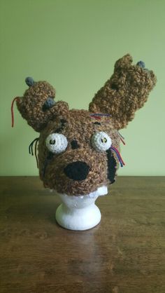 a crocheted dog head on top of a white vase sitting on a wooden table