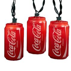 three coca - cola can lights are hanging from black corded ends on white background