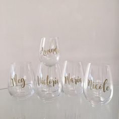 four wine glasses sitting on top of a glass table next to each other with gold lettering