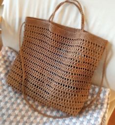 a brown crocheted bag sitting on top of a bed next to a pillow