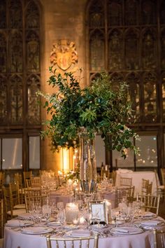 a tall vase filled with greenery sitting on top of a table covered in white linens