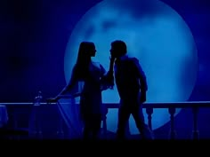 two people standing next to each other in front of a blue background with the moon behind them