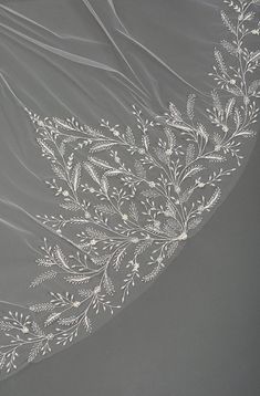 an embroidered veil with white flowers and leaves on the side, draped over a gray background