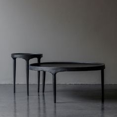 two black tables sitting next to each other on top of a cement floor in front of a white wall