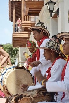 men in mexican garb playing drums on the street while others watch from behind them