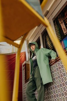 a woman leaning against a wall wearing a green coat