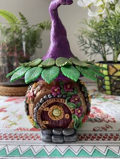 a purple gnome's house on top of a table next to potted plants